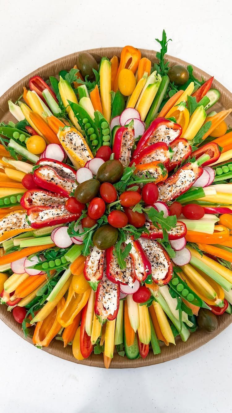 Vegetable platter with sliced peppers, carrots, celery, and cheese-stuffed red peppers on wood.