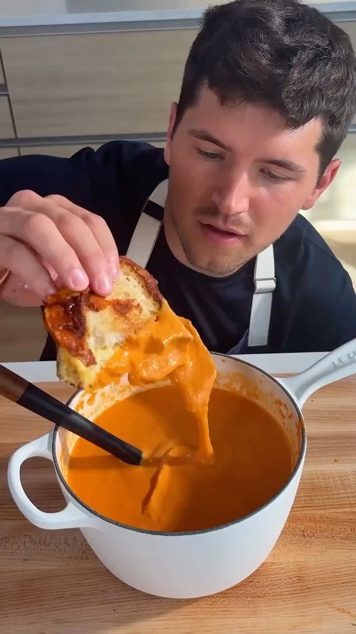 Grilled cheese sandwich being dipped into a pot of creamy tomato soup.