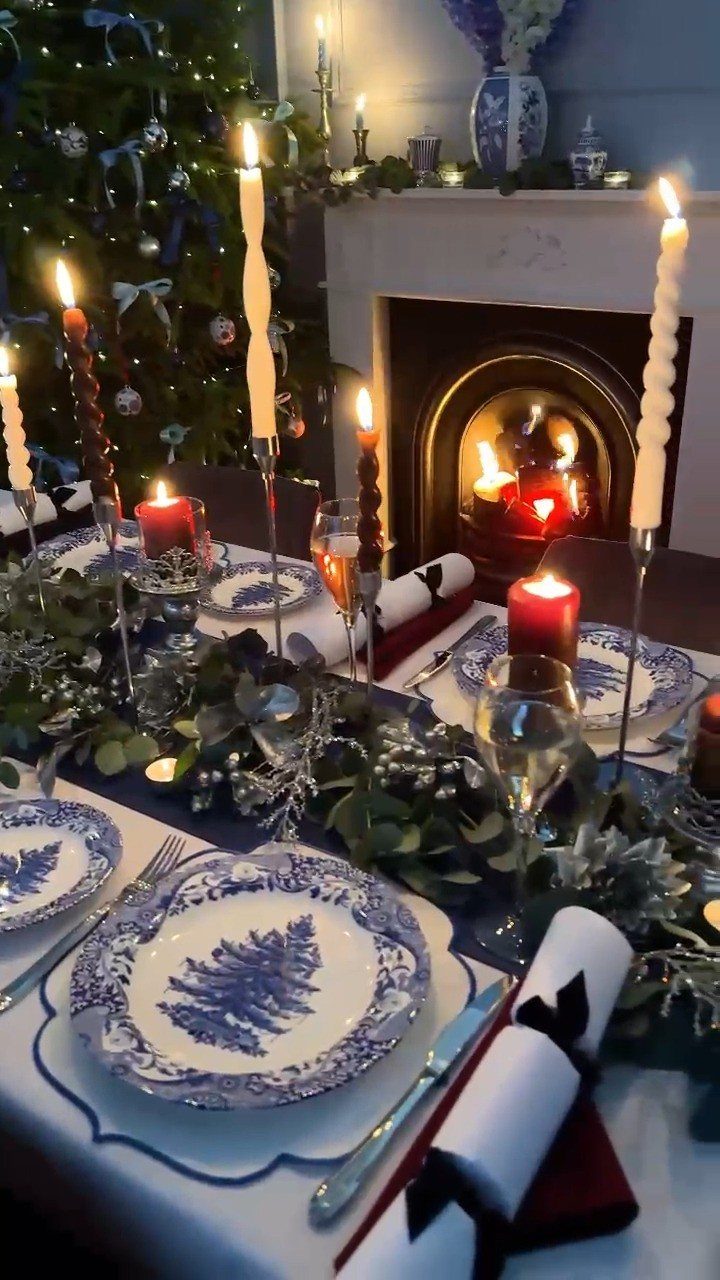 Blue and white patterned dinnerware on a festive table with candles and greenery.