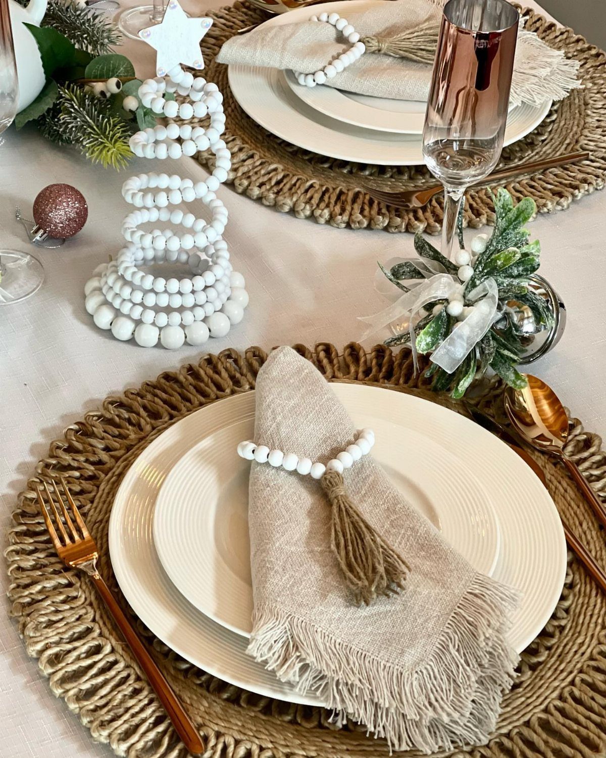 Beige linen napkin with a white beaded ring and tassel on a white plate.