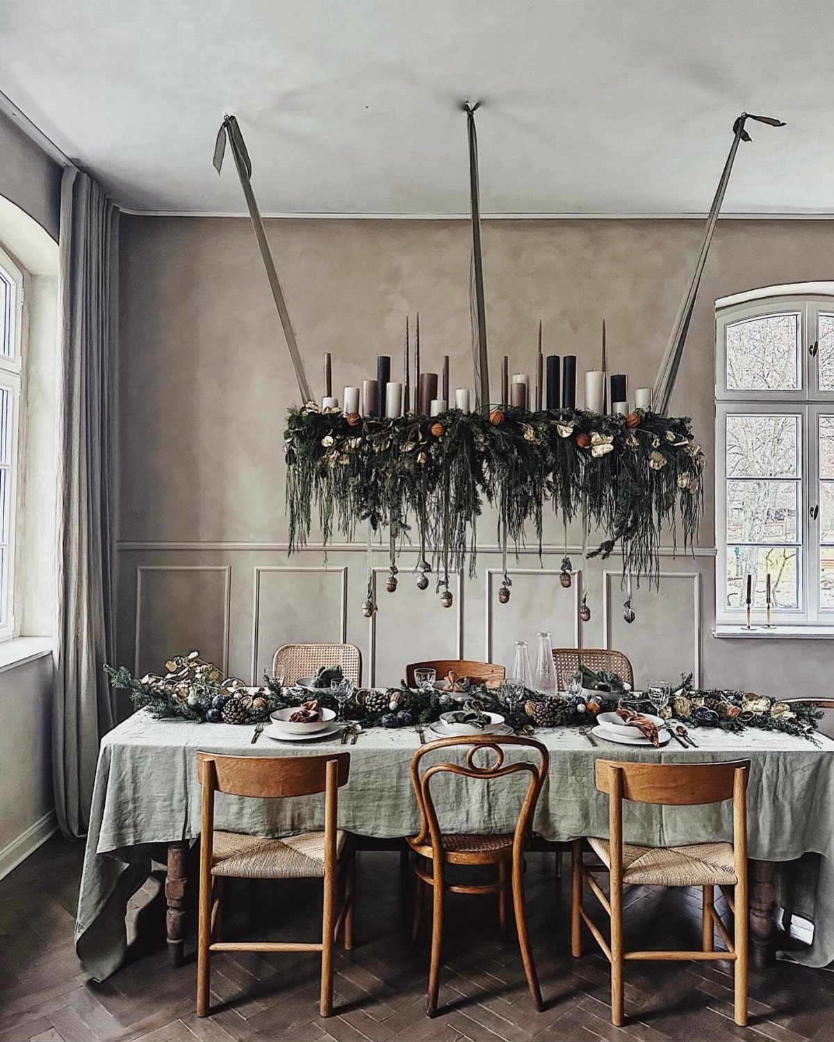 Dining table with greenery centerpiece and a hanging floral arrangement with white candles.