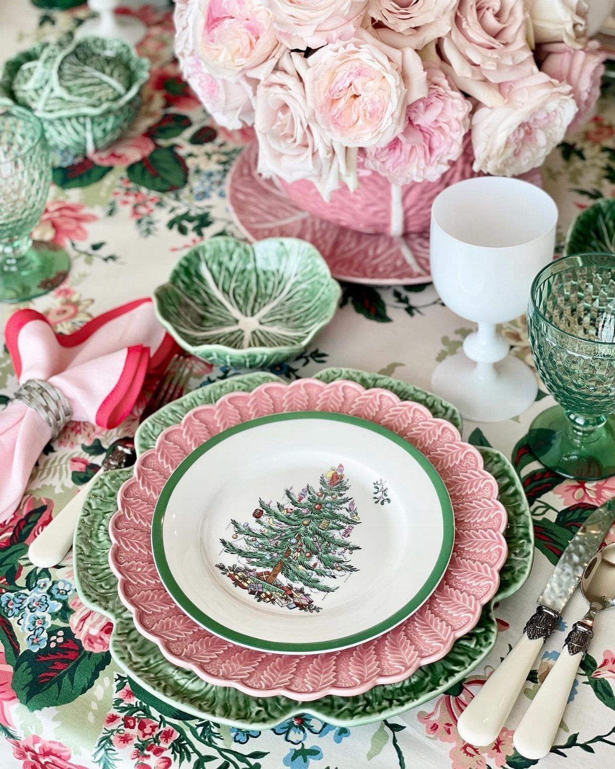 Mismatched pink and green plates with a Christmas tree center plate on floral tablecloth