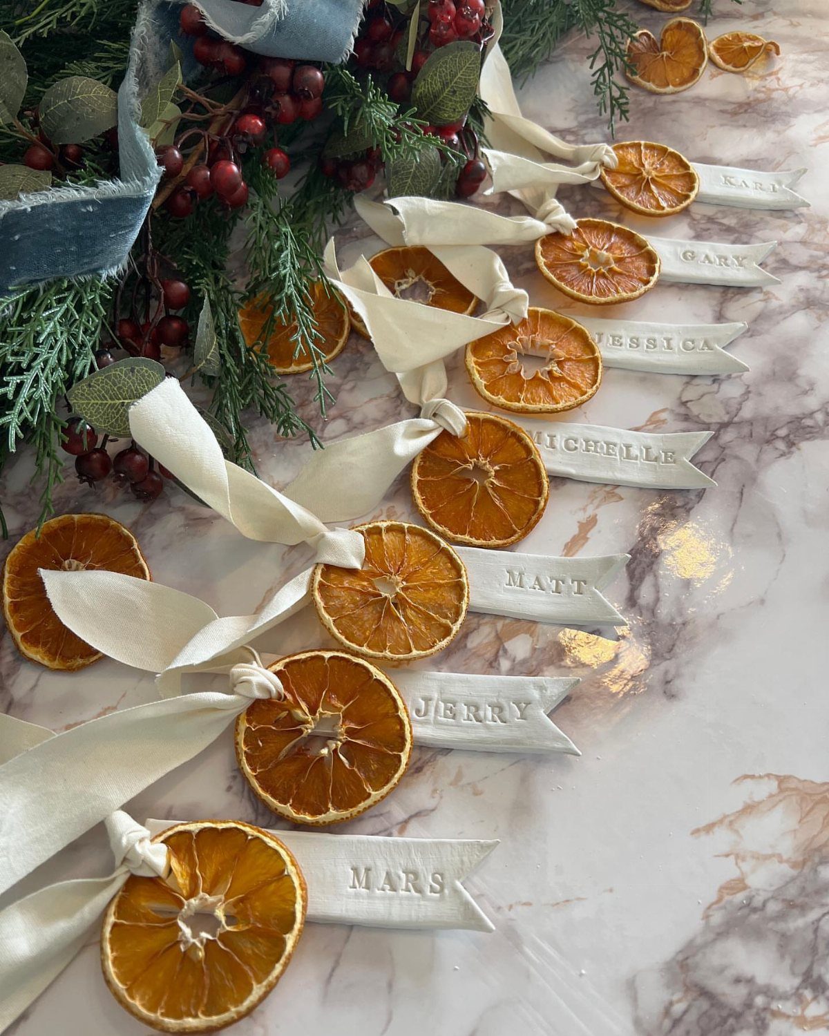 Dried orange slices and white name tags tied with ribbons on marble surface.