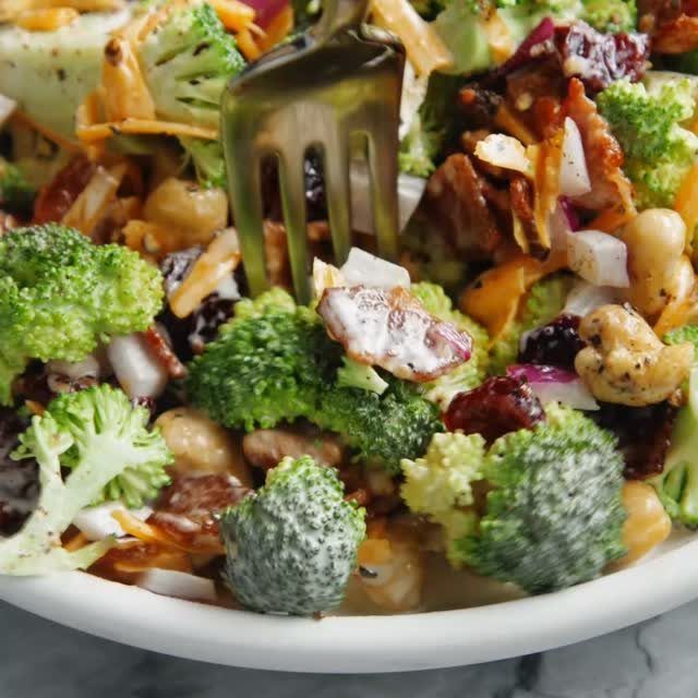 Broccoli salad with carrots, cranberries, and seeds being lifted by a gold fork.