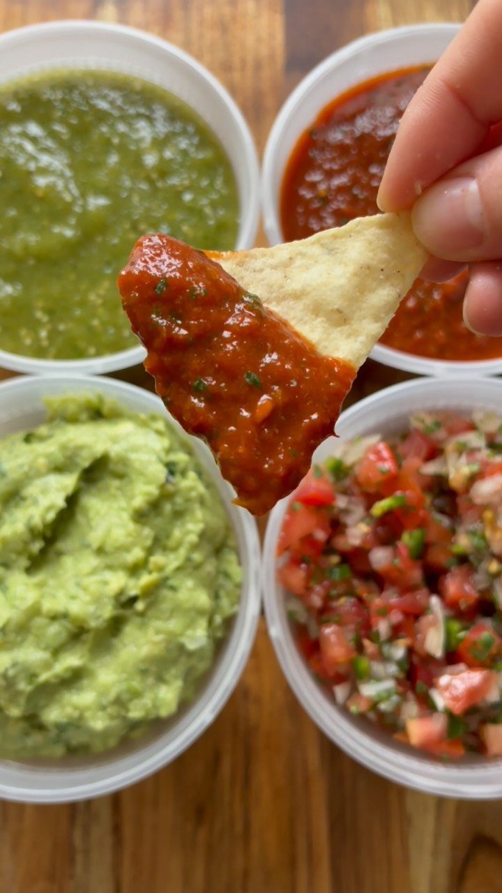 Four bowls of assorted salsas and guacamole with a dipped tortilla chip.