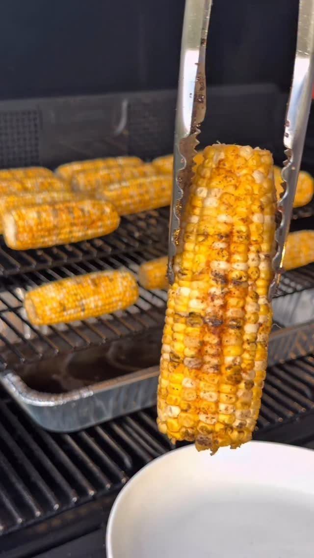 Grilled corn on the cob held by metal tongs over a barbecue grill