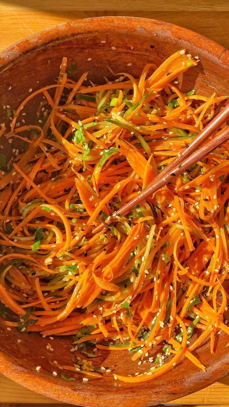 Shredded carrot salad with sesame seeds and herbs in a wooden bowl.