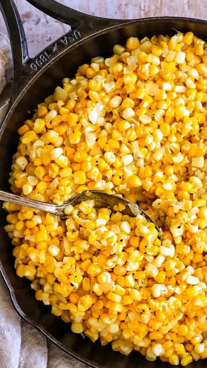Yellow corn kernels with onions in a black cast iron skillet with a spoon