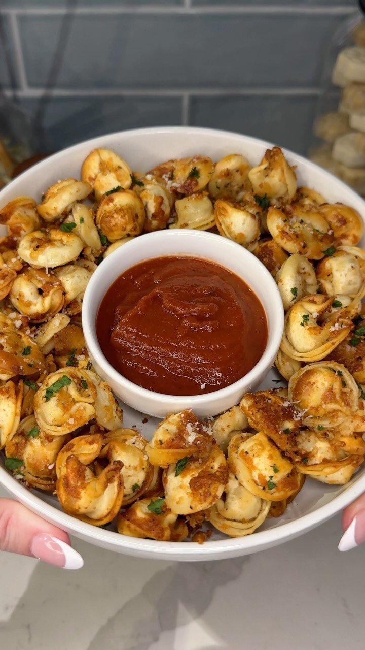 Seasoned tortellini pasta in a white bowl with a center dip of marinara sauce.