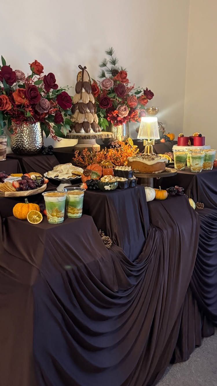 Dessert table with dark brown linens, red autumn flowers, and seasonal treats.