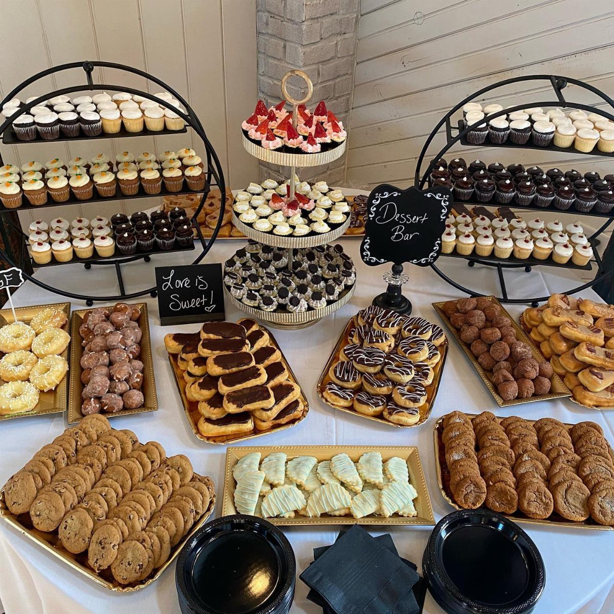 Dessert table with tiered cupcake stands, donuts, cookies, and a Dessert Bar sign.