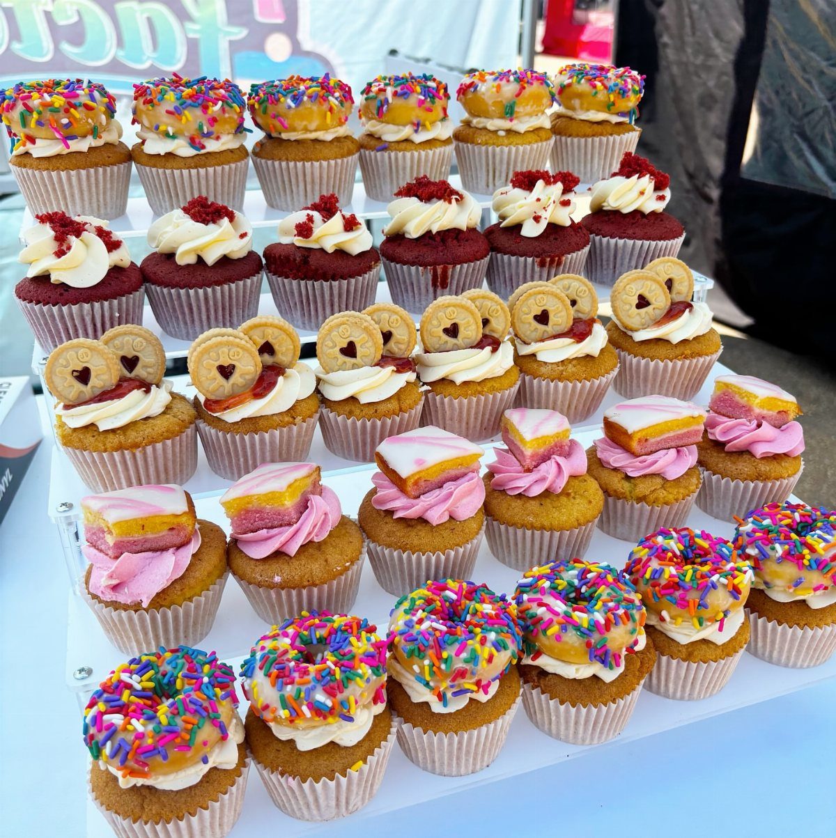 Assorted cupcakes with rainbow sprinkles, red velvet, and cookie toppings on a stand.