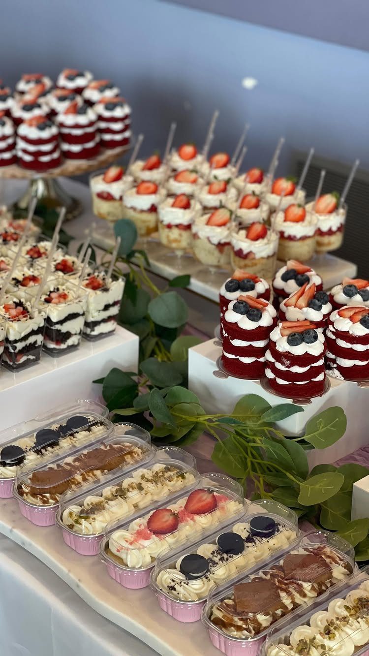 Red velvet cakes and strawberry parfaits arranged on a white dessert table with greenery.