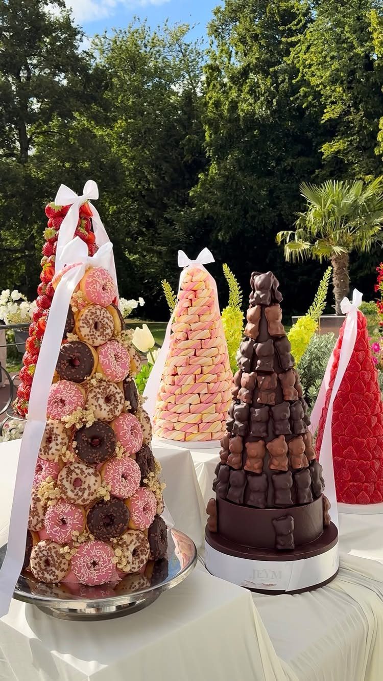 Four conical dessert towers with donuts, macarons, chocolate, and strawberries on a white table.