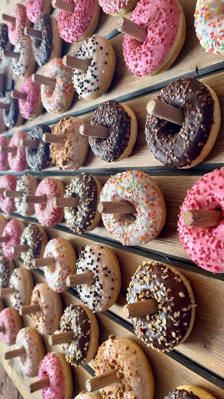 Assorted glazed donuts with sprinkles displayed on a wooden peg wall.