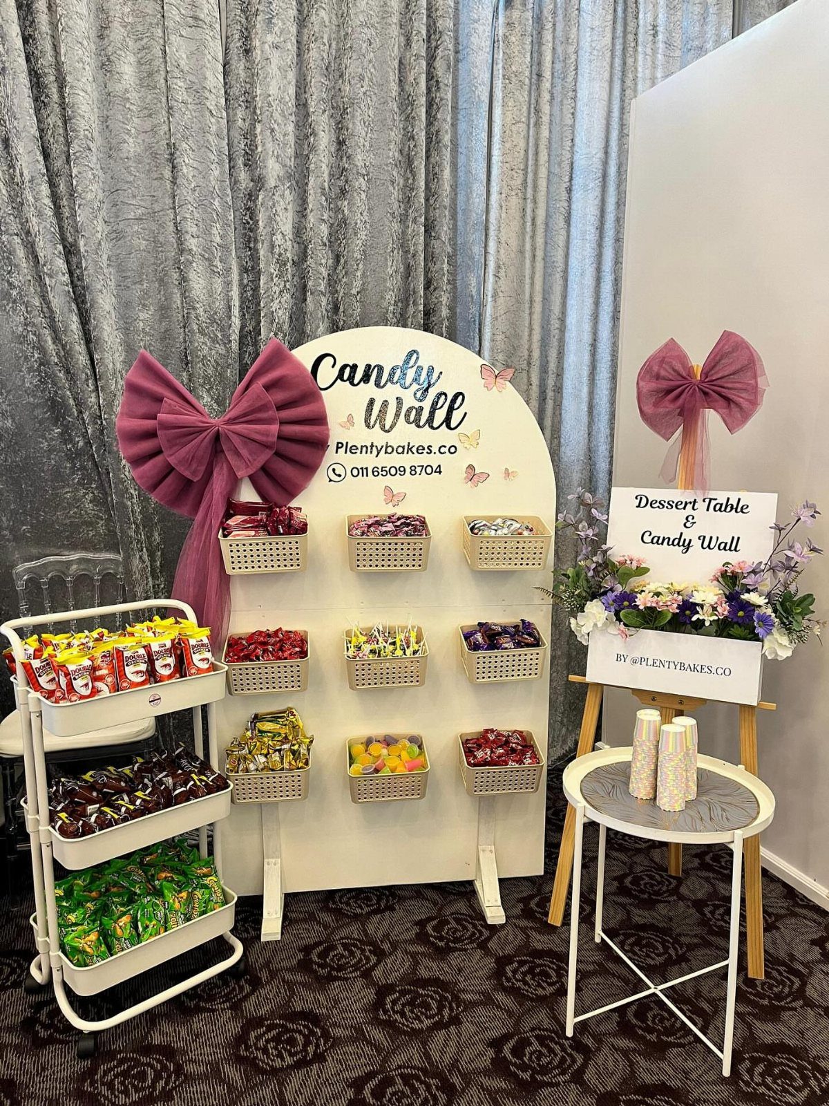 Candy wall and tiered cart filled with colorful sweets and purple bow decorations.