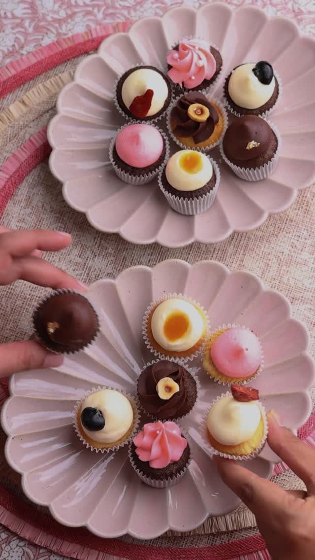 Mini cupcakes with colorful frosting on two pink scalloped plates being picked up.