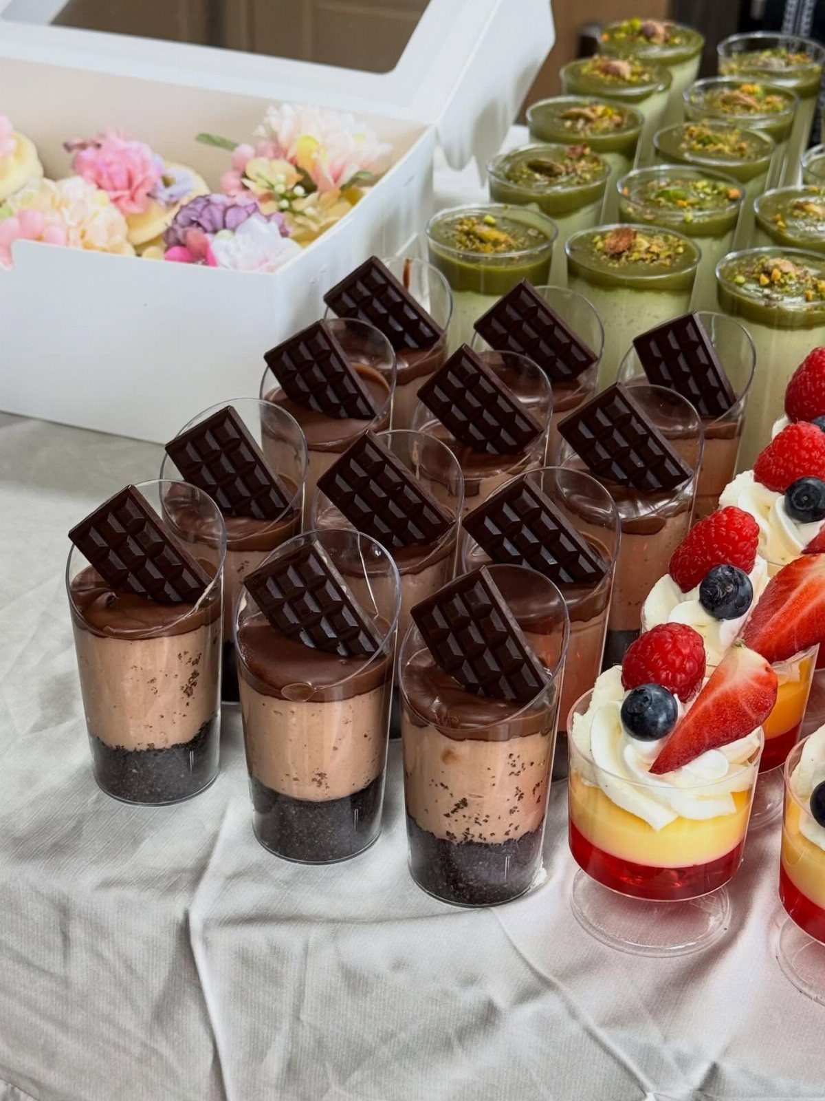 Mini dessert glasses with chocolate mousse, pistachio cream, and fruit parfaits on white fabric