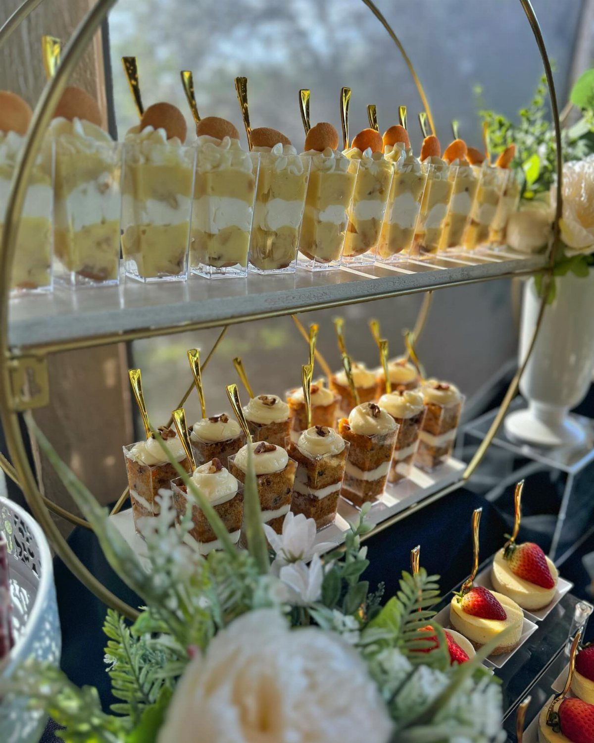 Two-tiered gold dessert stand with mini parfaits and cake cups and white flowers