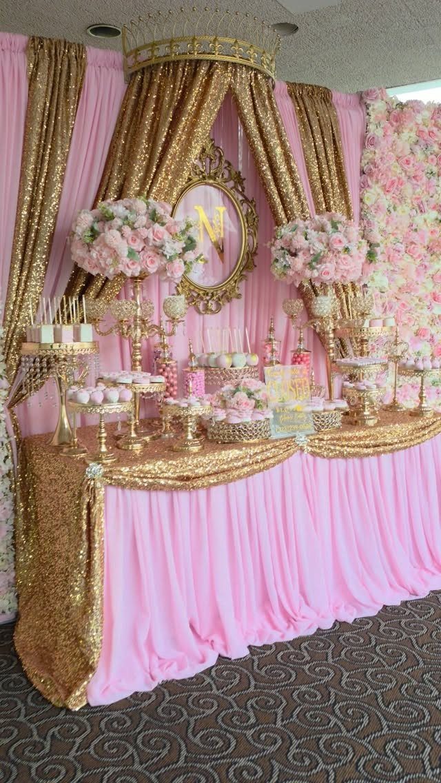 Pink and gold dessert table with sequin fabrics, cupcakes, and pink floral arrangements.