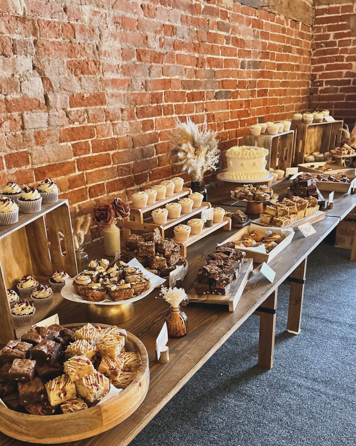 Assorted brownies, cupcakes, and a white cake on a rustic wooden dessert table.