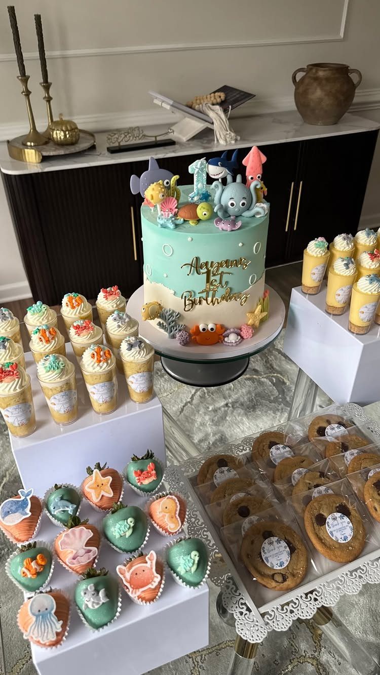 Ocean-themed dessert table with a blue cake, decorated strawberries, and mini cupcakes.
