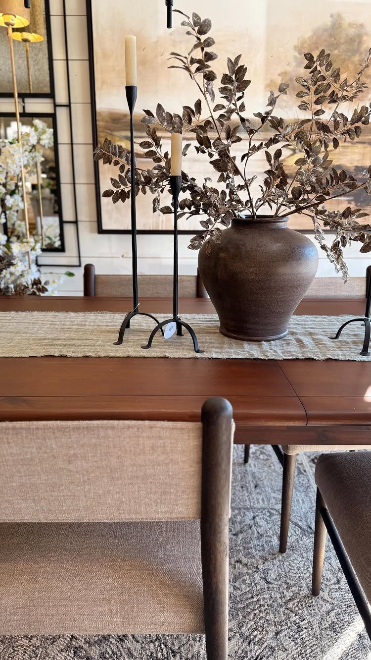 Wooden dining table decorated with a ceramic vase, dried branches, and black candlesticks.