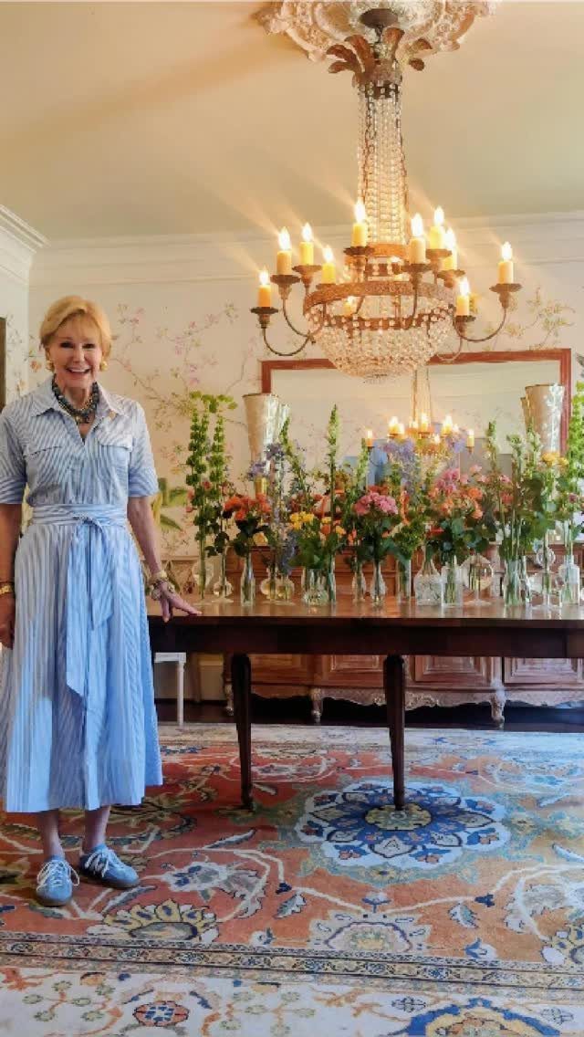 Woman standing by a dining table decorated with many vases of colorful fresh flowers.