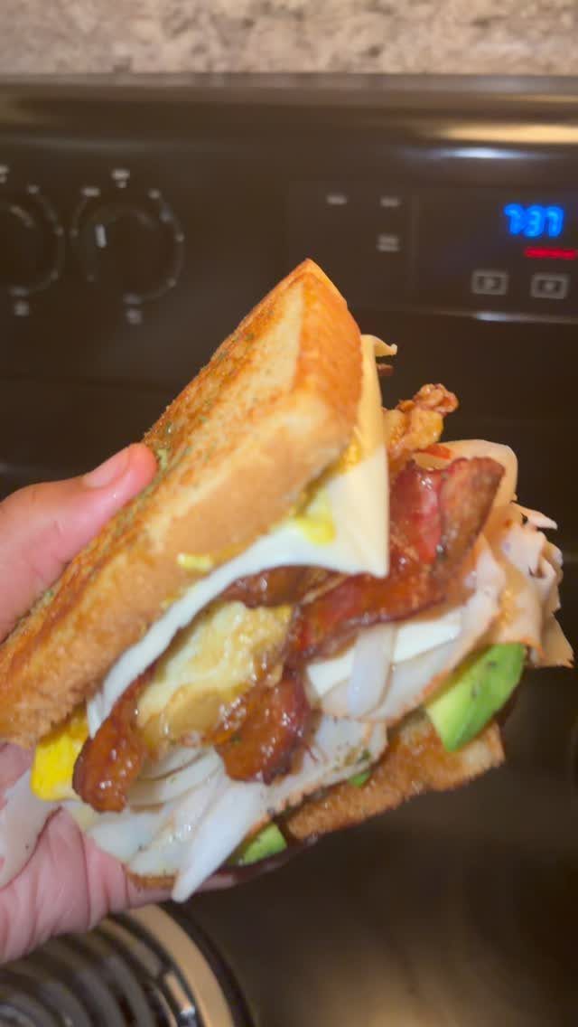Toasted sandwich with chicken, bacon, Swiss cheese, and avocado held in a hand.