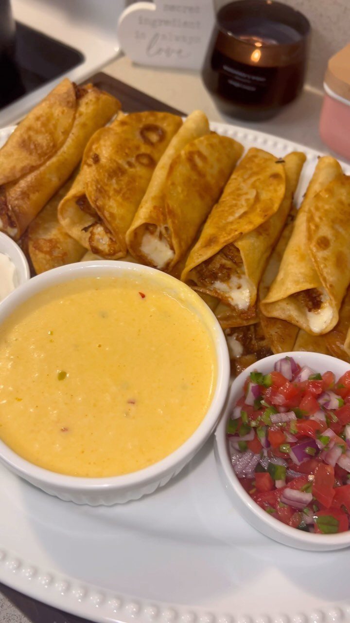 Golden-brown chicken taquitos on a white platter with cheese sauce and fresh salsa.