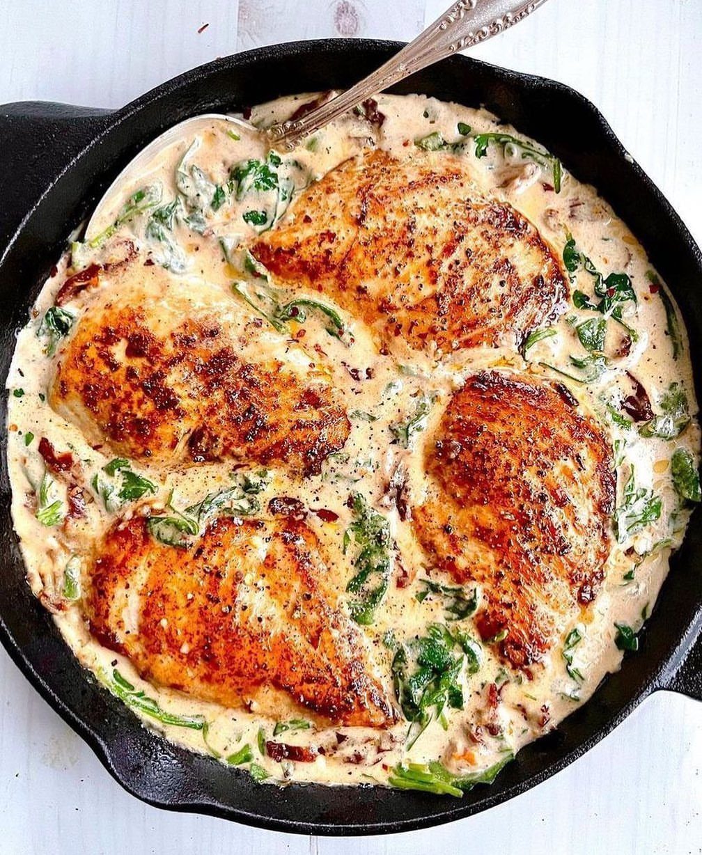 Seared chicken breasts in a creamy sauce with spinach and sun-dried tomatoes in skillet