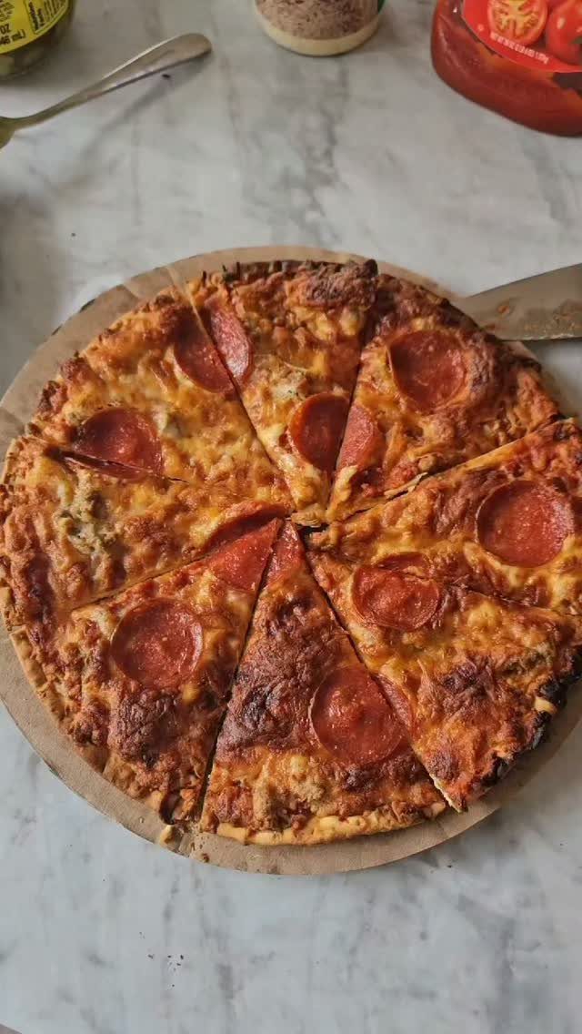 Pepperoni pizza sliced into wedges on a cardboard base over marble surface