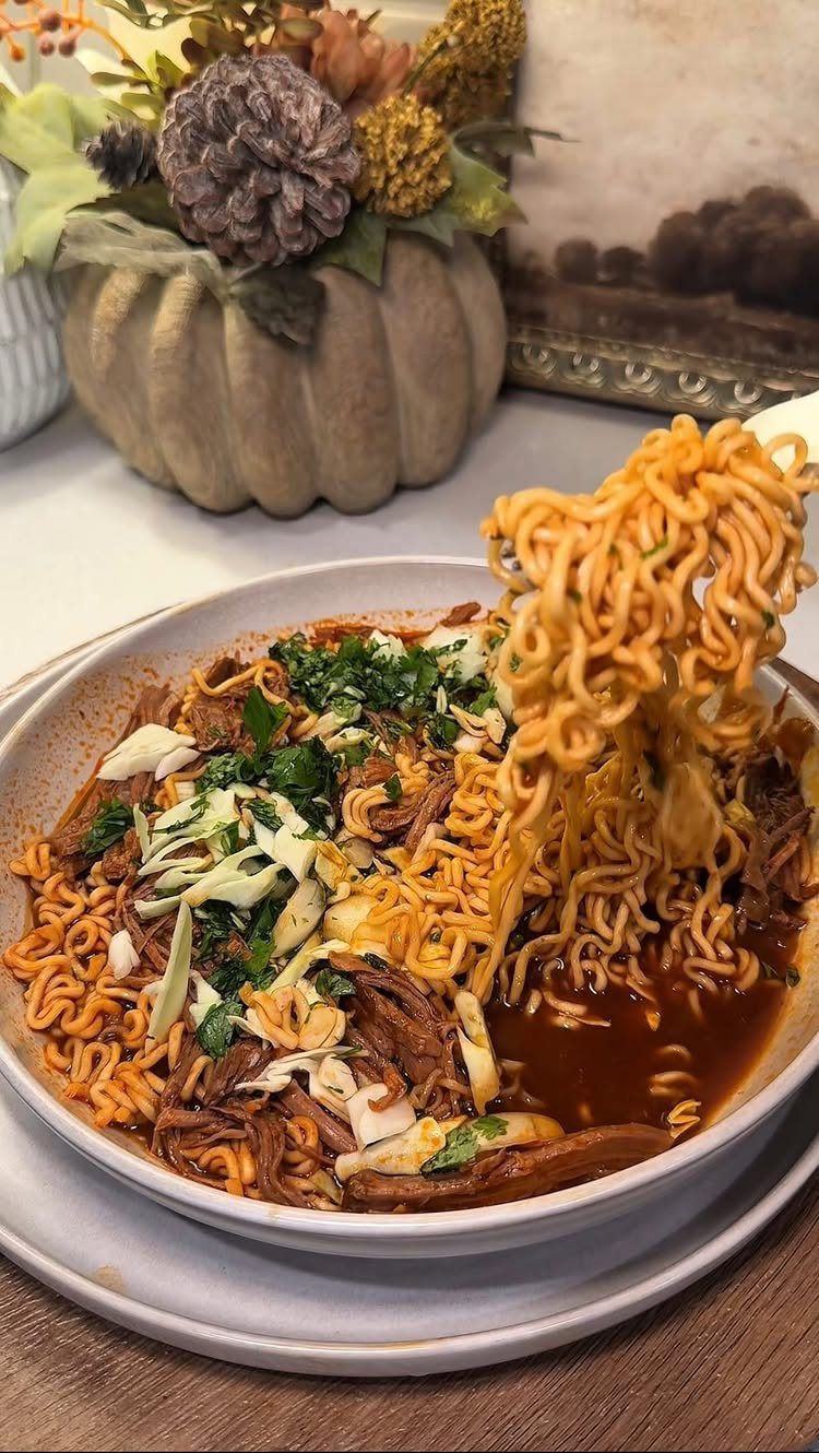 Ramen noodles with shredded beef and green onions in a white bowl.
