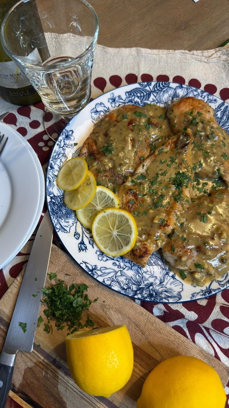 Creamy chicken piccata with lemon slices on a blue and white patterned plate.