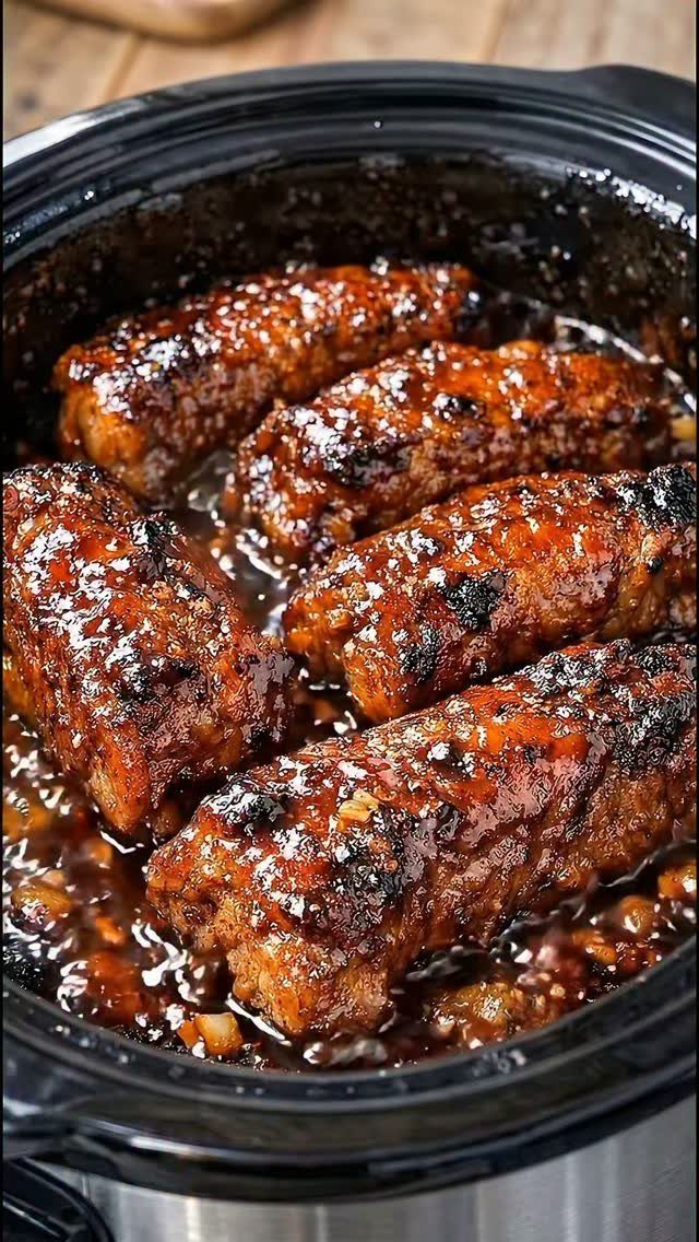 Mini barbecue meat loaves glazed in sauce inside a black slow cooker pot.