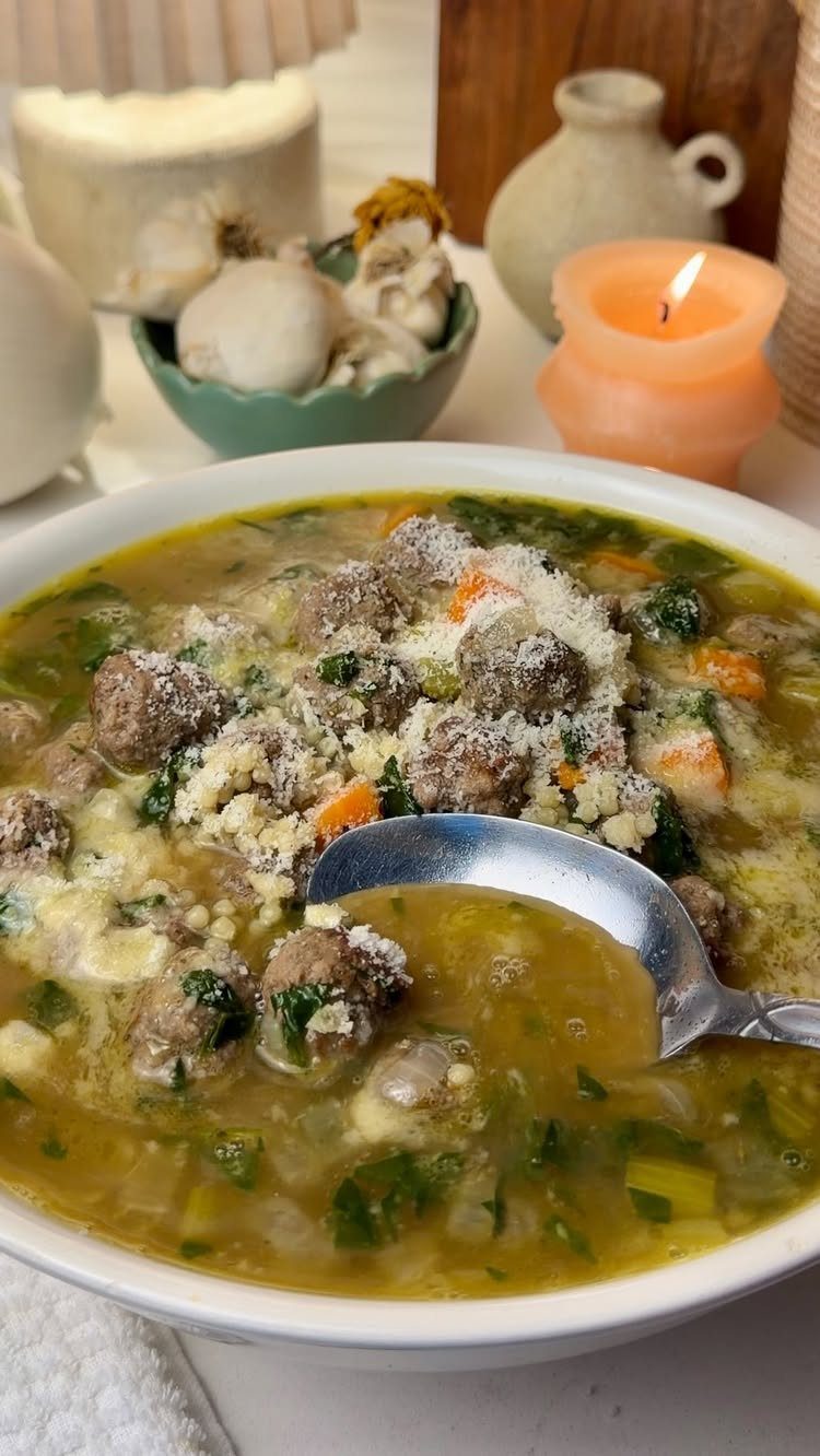 Beef meatball and spinach soup with grated cheese in a white bowl