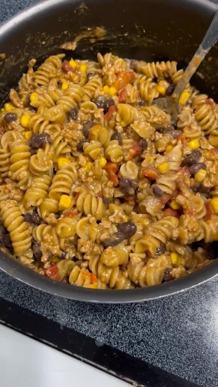 Rotini pasta with ground meat, black beans, and corn in a black pot.