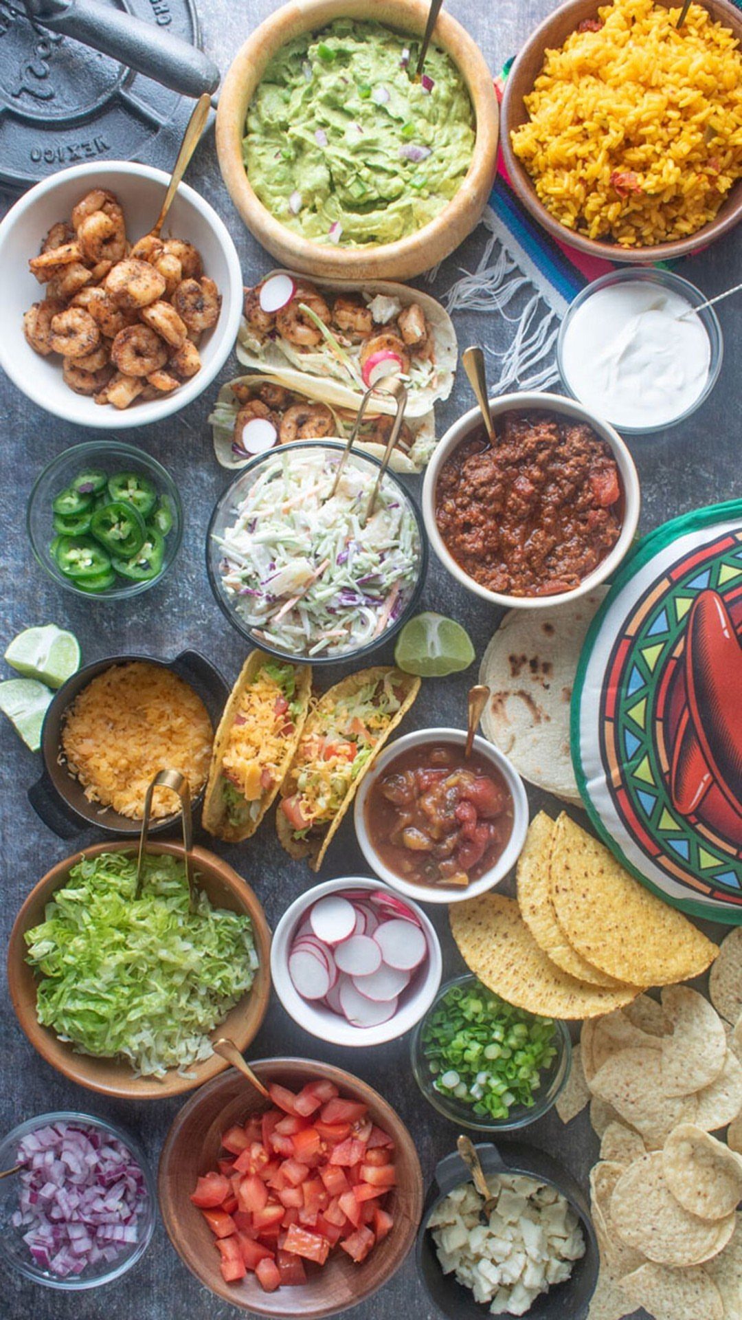 Taco bar spread with various toppings, bowls of guacamole, rice, and corn tortillas.
