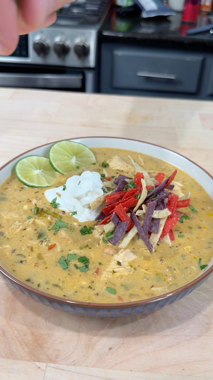 Creamy white chili in a bowl topped with tortilla strips, sour cream, and lime.