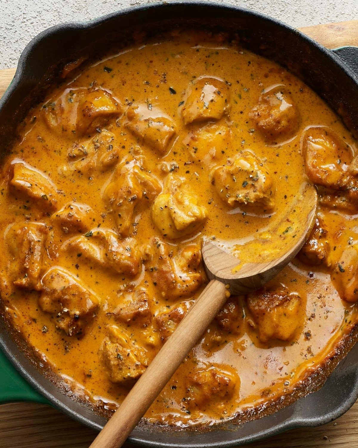 Chicken butter curry in a black cast iron skillet with a wooden spoon.