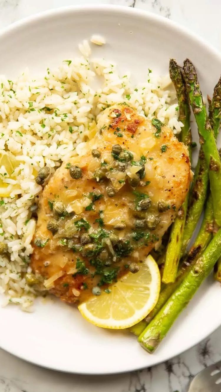 Chicken breast with caper lemon sauce, white rice, and roasted asparagus on a plate.