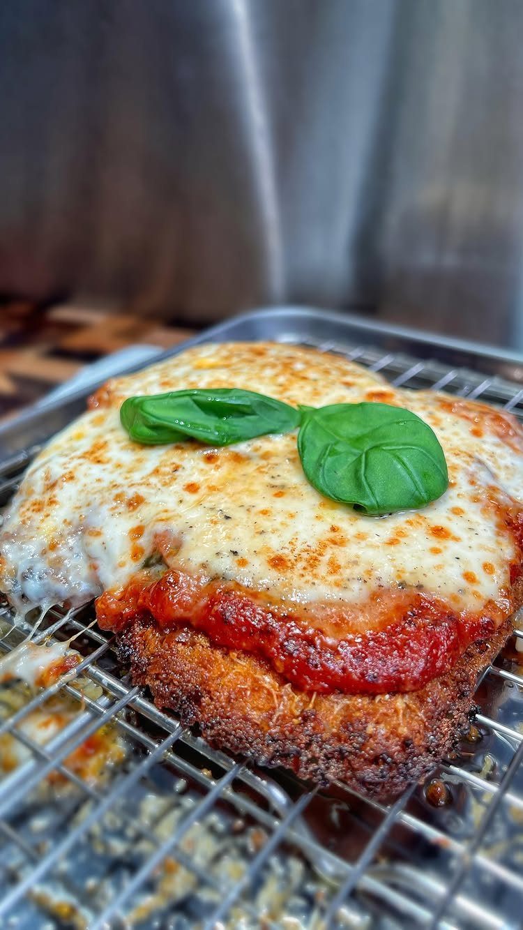 Breaded mozzarella schnitzel topped with tomato sauce and basil on a wire rack.