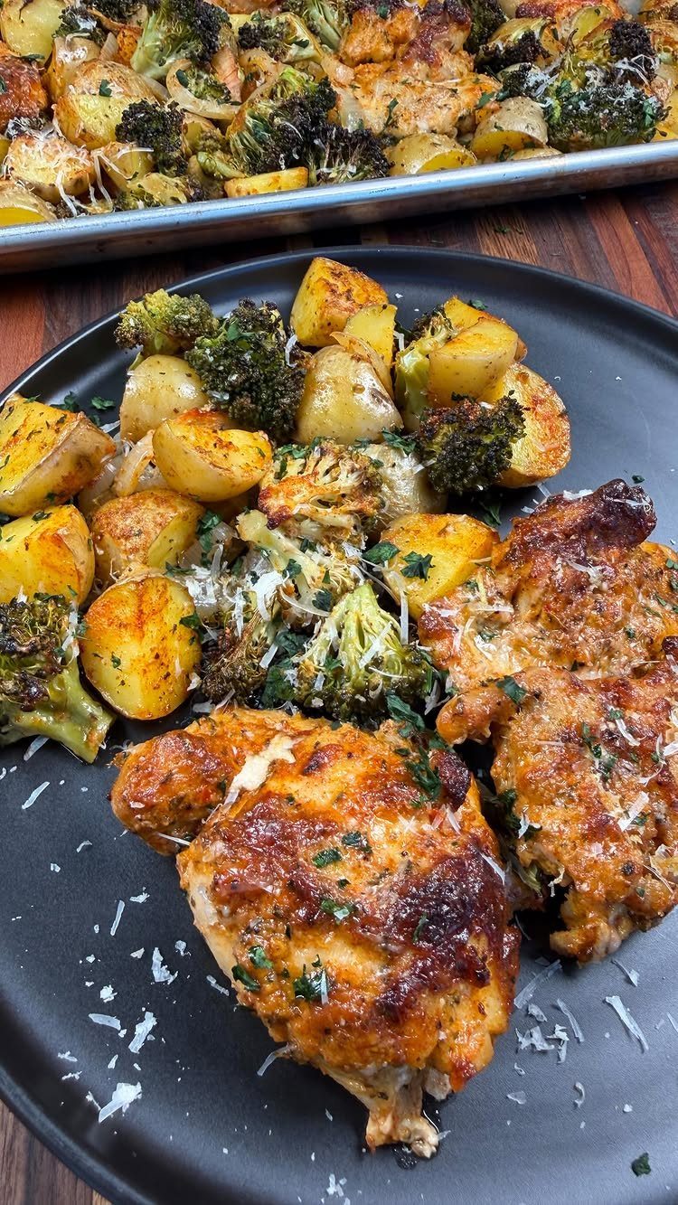 Roasted chicken thighs and potatoes with broccoli served on a black plate.