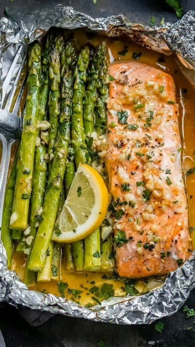 Salmon fillet and asparagus spears seasoned with garlic in a foil packet.