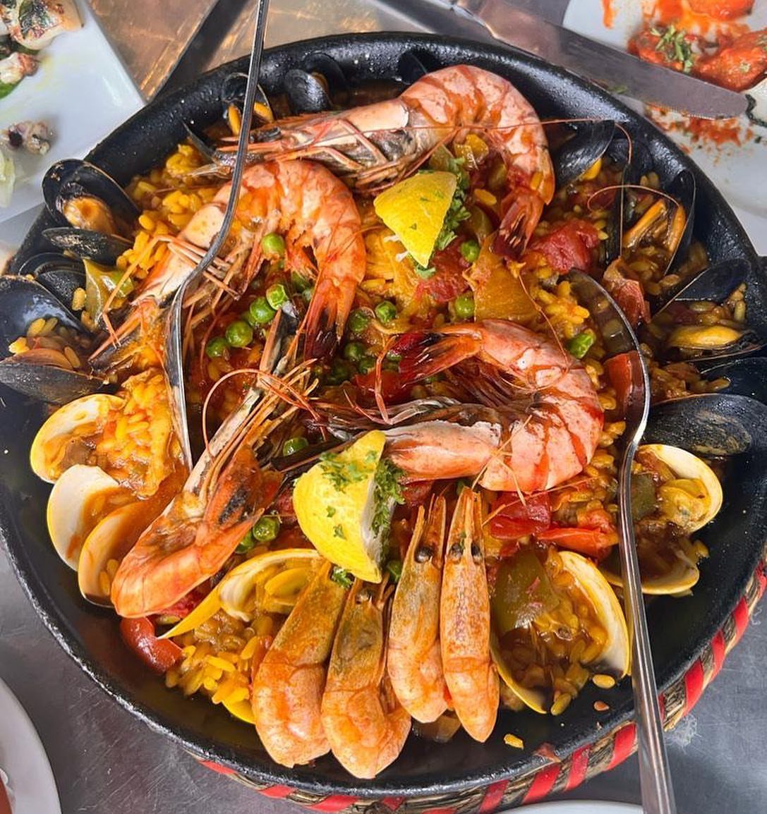 Classic paella with prawns, mussels, and clams served in a black pan.