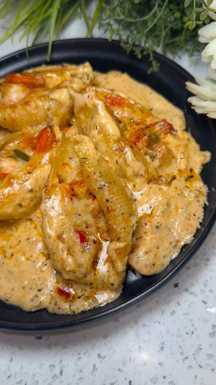 Stuffed pasta shells in a creamy orange Cajun sauce on a black plate.