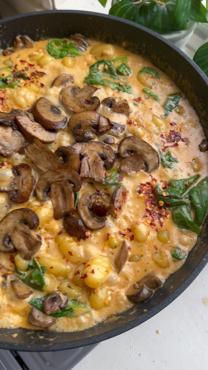 Gnocchi in creamy sauce with sliced mushrooms and spinach in a black skillet