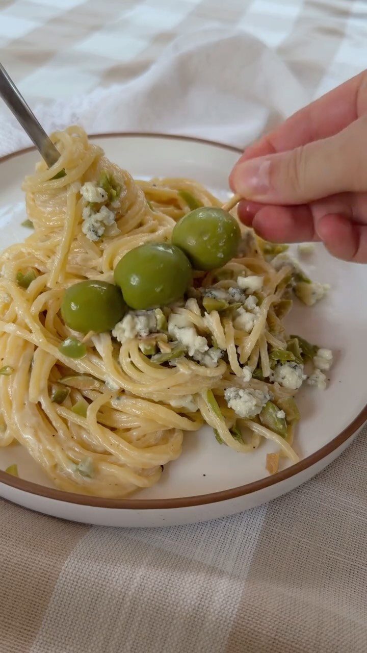 Creamy spaghetti pasta topped with green olives and crumbled cheese on a plate.
