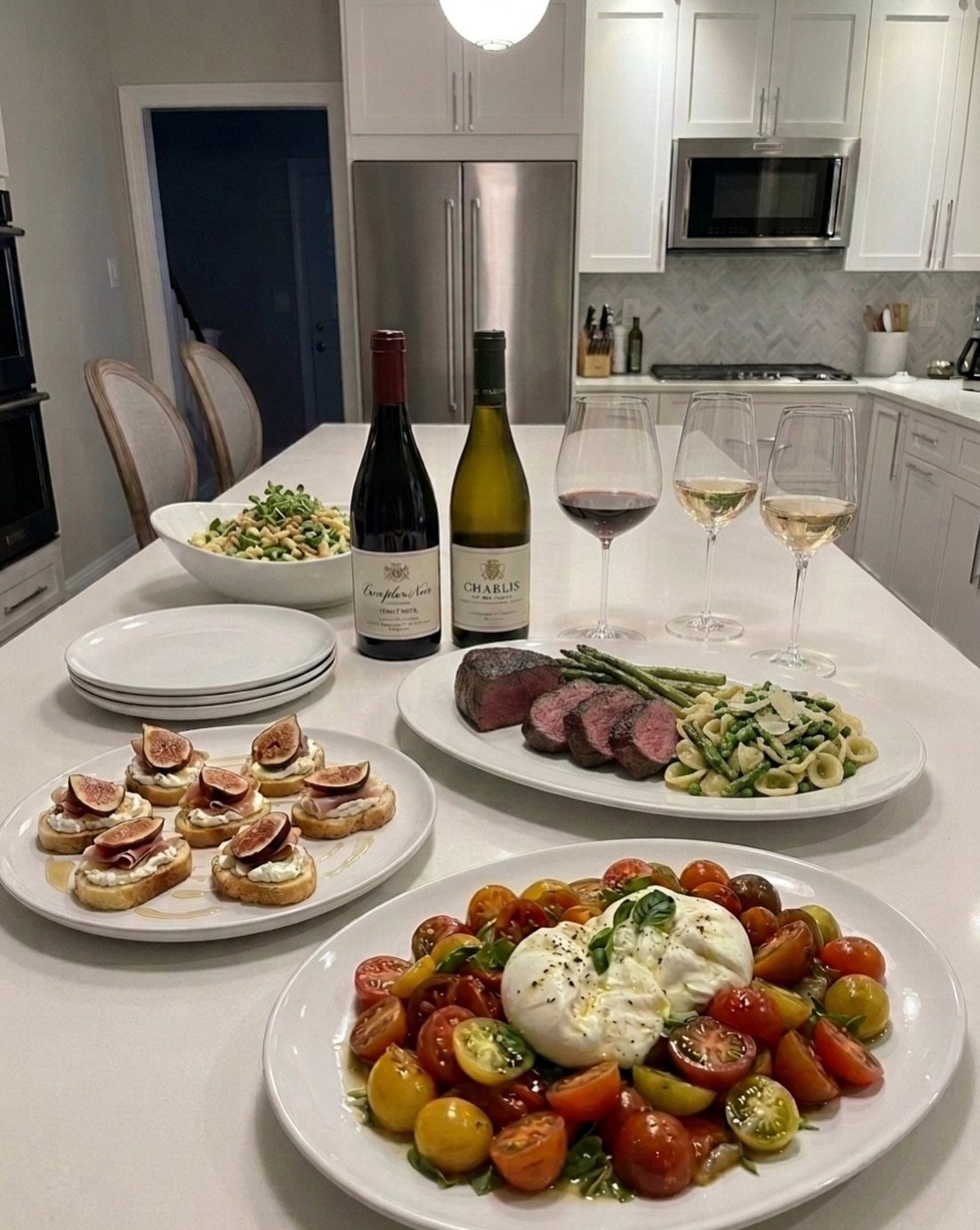 Dinner spread on a white counter with Caprese salad, steak, and wine.