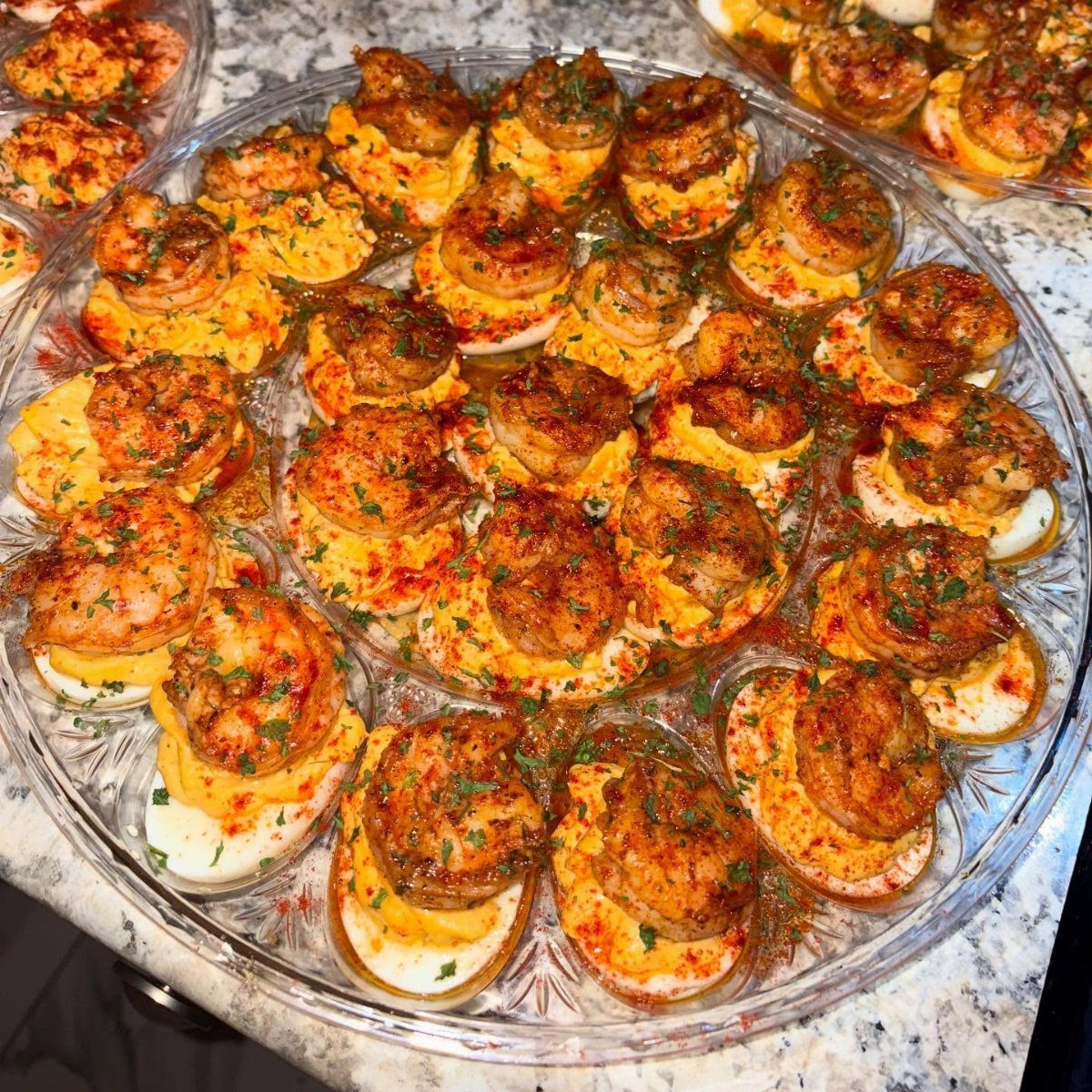 Deviled eggs topped with seasoned shrimp and herbs on a glass platter.